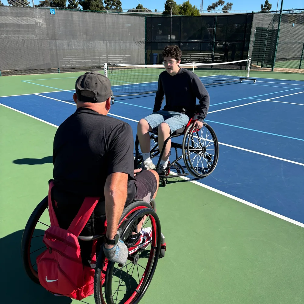 Two wheelchair players facing each other on a pickleball court during the test session